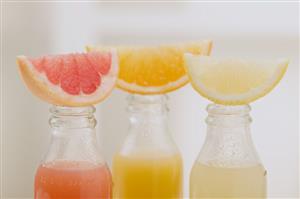 Three fruit juices in bottles with wedges of fresh fruit