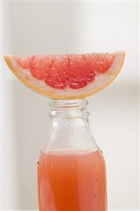 Pink grapefruit juice in bottle with fresh grapefruit wedge