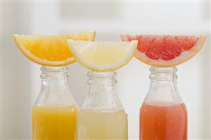 Three fruit juices in bottles with wedges of fresh fruit