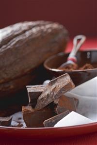 Pieces of chocolate in front of cocoa powder & cacao fruit