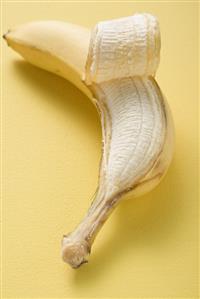 Banana, partly peeled, on yellow background