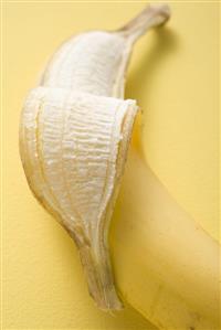 Banana, partly peeled, on yellow background