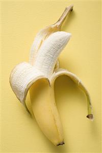 Banana, half peeled, on yellow background