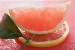 Wedge of pink grapefruit on slice of grapefruit with leaf