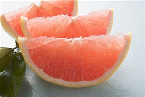 Three pink grapefruit wedges, leaves beside them