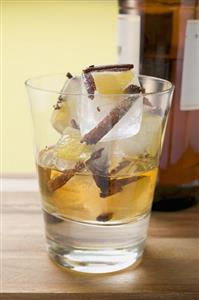 Rum and ice cubes with spices and pieces of fruit in glass