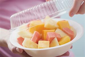 Woman removing lid from plastic dish of exotic fruit salad