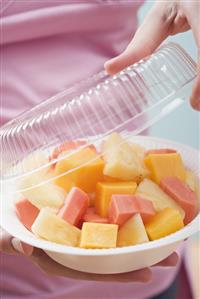 Woman removing lid from plastic dish of exotic fruit salad