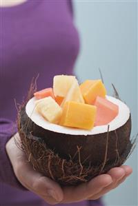 Woman holding hollowed-out coconut full of exotic fruit salad