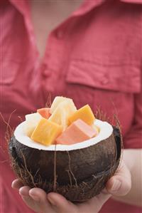 Woman holding hollowed-out coconut full of exotic fruit salad