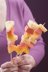 Woman holding three exotic fruit skewers