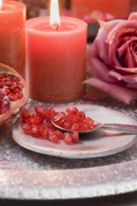 Pomegranate seeds on plate with spoon, red candles & rose