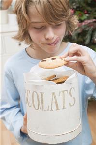 Boy taking chocolate chip cookie out of cookie tin