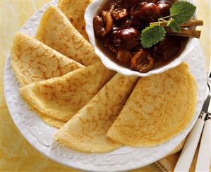 Several folded crepes with a bowl of cherries