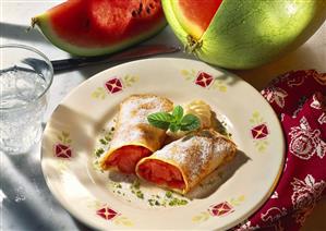 Crepes with watermelon filling, icing sugar and cream on plate