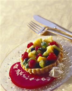 Colourful fruit tartlet on red sauce, on glass plate