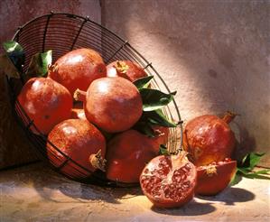 Whole Pomegranates in a Wire Basket; One Cut in Half