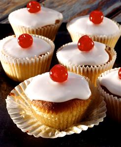 Iced muffins with cherries on top in paper cases