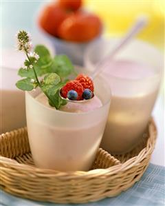 Berry milk shake in glasses on tray, spoon with berries above