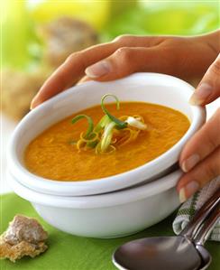 Hands holding a bowl of carrot soup