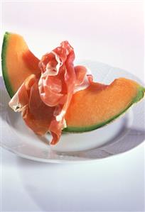 A piece of netted melon with raw ham on plate