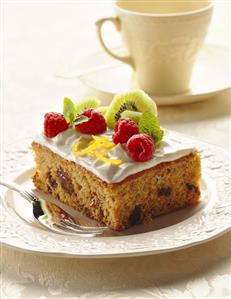 A piece of spice cake with white icing, raspberries & kiwi