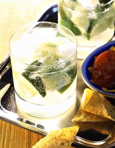 A glass of Caipirinha on tray with nachos and dip