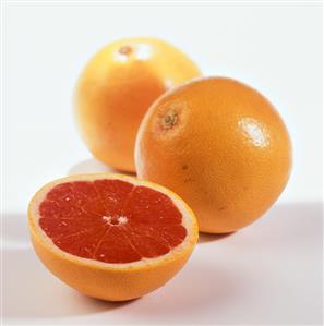 Half a pink grapefruit in front of two whole ones
