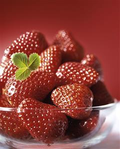 Strawberries in glass bowl against red background