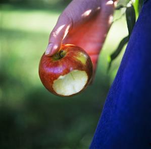 Apple, a bite taken, in someone's hand in open air