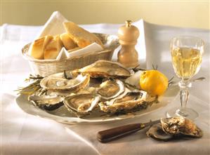 A plate of oysters, with lemon, baguette and wine