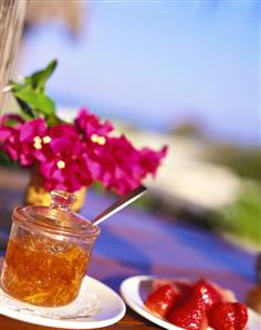 A jar of orange marmalade, in background flowers & sea