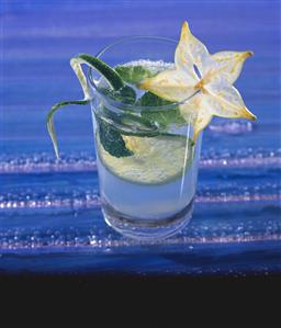 A glass of water with lemon, lemon spiral and carambola