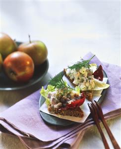 Two black bread triangles with herring salad, apples beside it