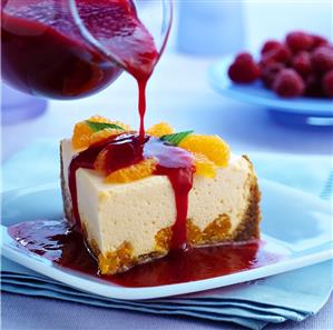 Pouring raspberry sauce over orange cream gateau