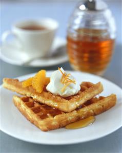 Orange waffles with cream and maple syrup and a cup of tea