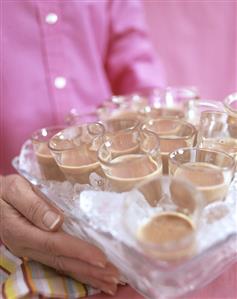 Hands holding tray with glasses of ice-cold chocolate liqueur