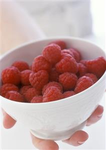 Hand holding a bowl of fresh raspberries