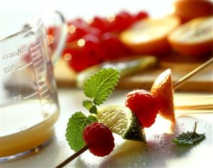 Still life with fruit kebab, juice in measuring jug & fruit