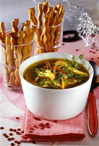 Chicken soup with vegetables, bread sticks in glasses behind