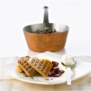 Heart-shaped waffles with hot cherries and cream