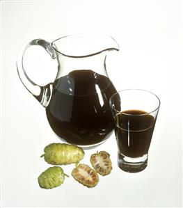 Noni juice in carafe and glass, noni fruits in front (1)