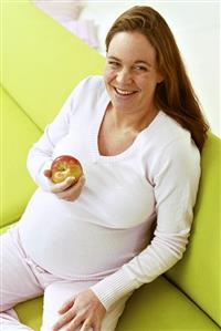 Pregnant woman on sofa eating an apple