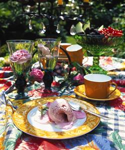 Summery table laid for coffee with roses, fruit and ice cream