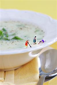 Miniature cleaning ladies scrubbing edge of plate of leek soup