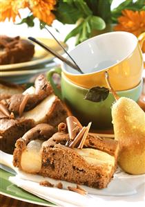 Chocolate pear cake on plate; fresh pear, coffee cups