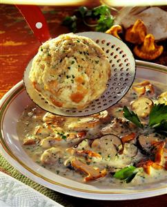 Mushroom soup with bread dumplings in a ladle over a plate