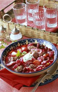 Bortsch in deep plate in front of tray of glasses