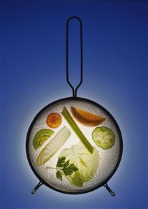 Vegetables, salad leaves & fruit slices under a strainer