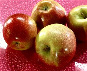 Braeburn apples on a pink background with water drops